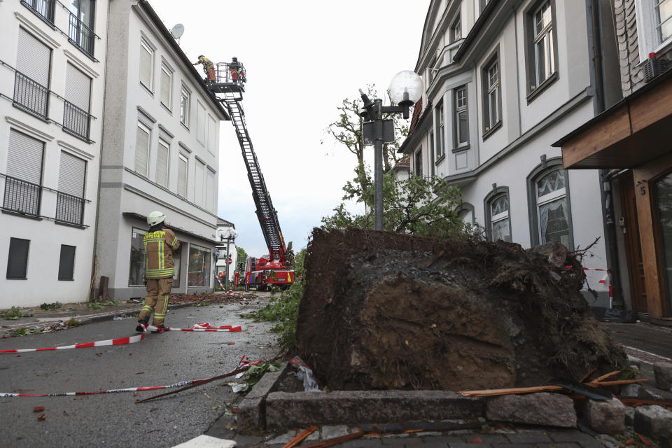 Firefighters stand on a turntable ladder truck removing damaged remnants of a roof, in Lippstadt, Germany, Friday, May 20, 2022. In the foreground lies a fallen tree. A suspected tornado caused massive damage in Lippstadt on Friday afternoon. (Friso Gentsch/dpa via AP)