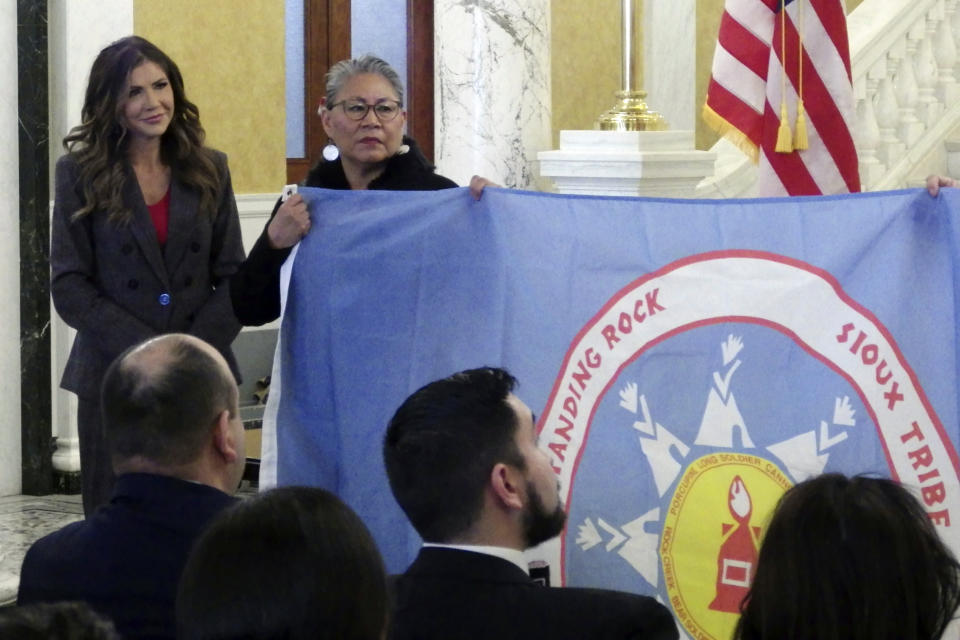 South Dakota Republican Gov. Kristi Noem, left, and Standing Rock Sioux Tribal Chairwoman Janet Alkire stand during a ceremony in which tribal leaders presented flags of the Standing Rock and Rosebud Sioux tribes, Wednesday, Jan. 10, 2024, at the state Capitol in Pierre, S.D. Alkire is holding the Standing Rock flag. (AP Photo/Jack Dura)