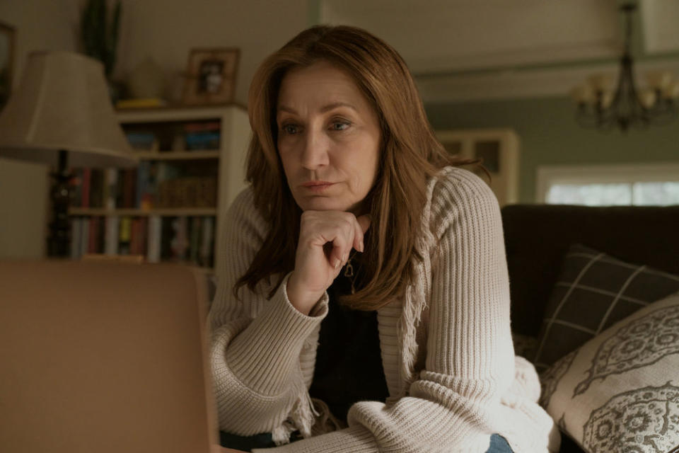 A woman in a beige knit cardigan sits on her living room sofa, her hand at her chin in deep thought; Edie Falco in "Bupkis"