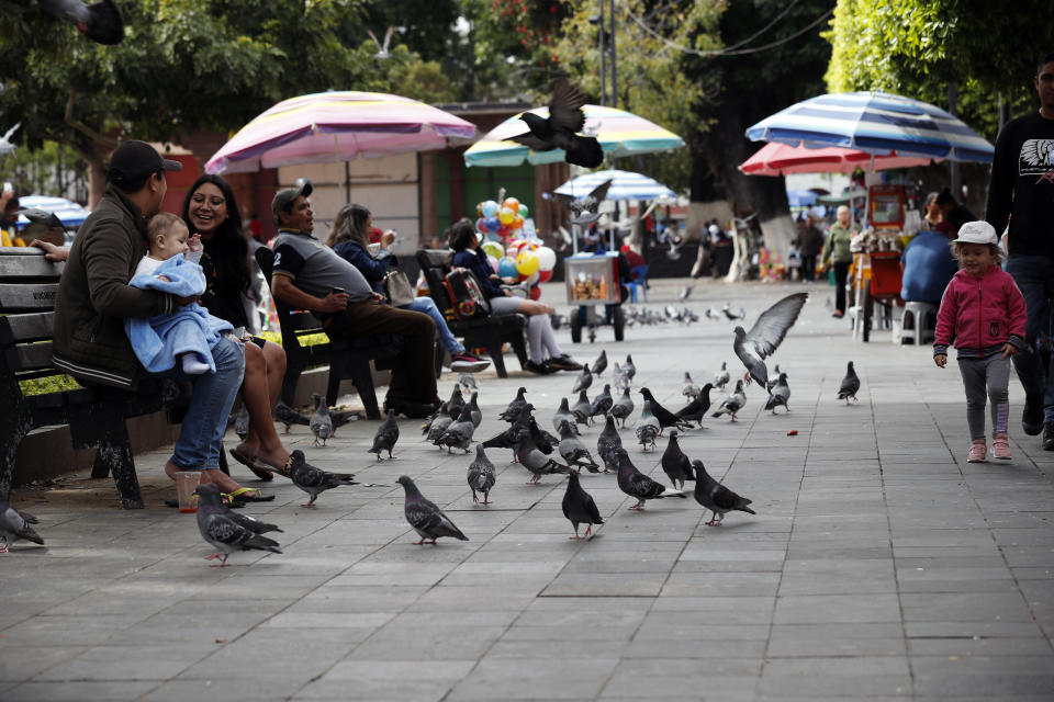 In this Feb. 6, 2020 photo, residents sit on benches in the city square in Uruapan, Michoacan state, Mexico. Uruapan, a city of about 340,000 people, is in Mexico's avocado belt, where violence has reached shocking proportions. In Uruapan, cartels are battling for territory and reports of killings are common, such as the gun massacre last week of three young boys, a teenager and five others at an arcade in what had been a relatively quiet neighborhood. (AP Photo/Marco Ugarte)