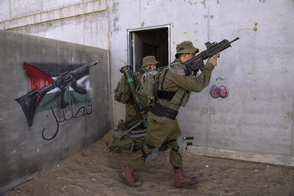 Israeli soldier carry ammunition next to a graffiti featuring the Palestinian flag, during an urban warfare exercise at an army training facility at the Zeelim army base, southern Israel, May 25, 2022. Officially, the site is known as the Urban Warfare Training Center. But to soldiers, it is known as Mini Gaza, simulating a Palestinian urban area with 500 buildings and narrow alleyways adorned with murals and posters honoring slain fighters. The training center can accommodate exercises for an entire brigade of 2,000 soldiers at once. (AP Photo/Oded Balilty)