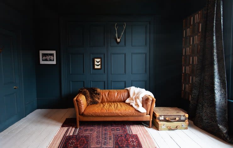 a-leather-couch-sits-in-front-of-a-dark-green-wall-with-texture