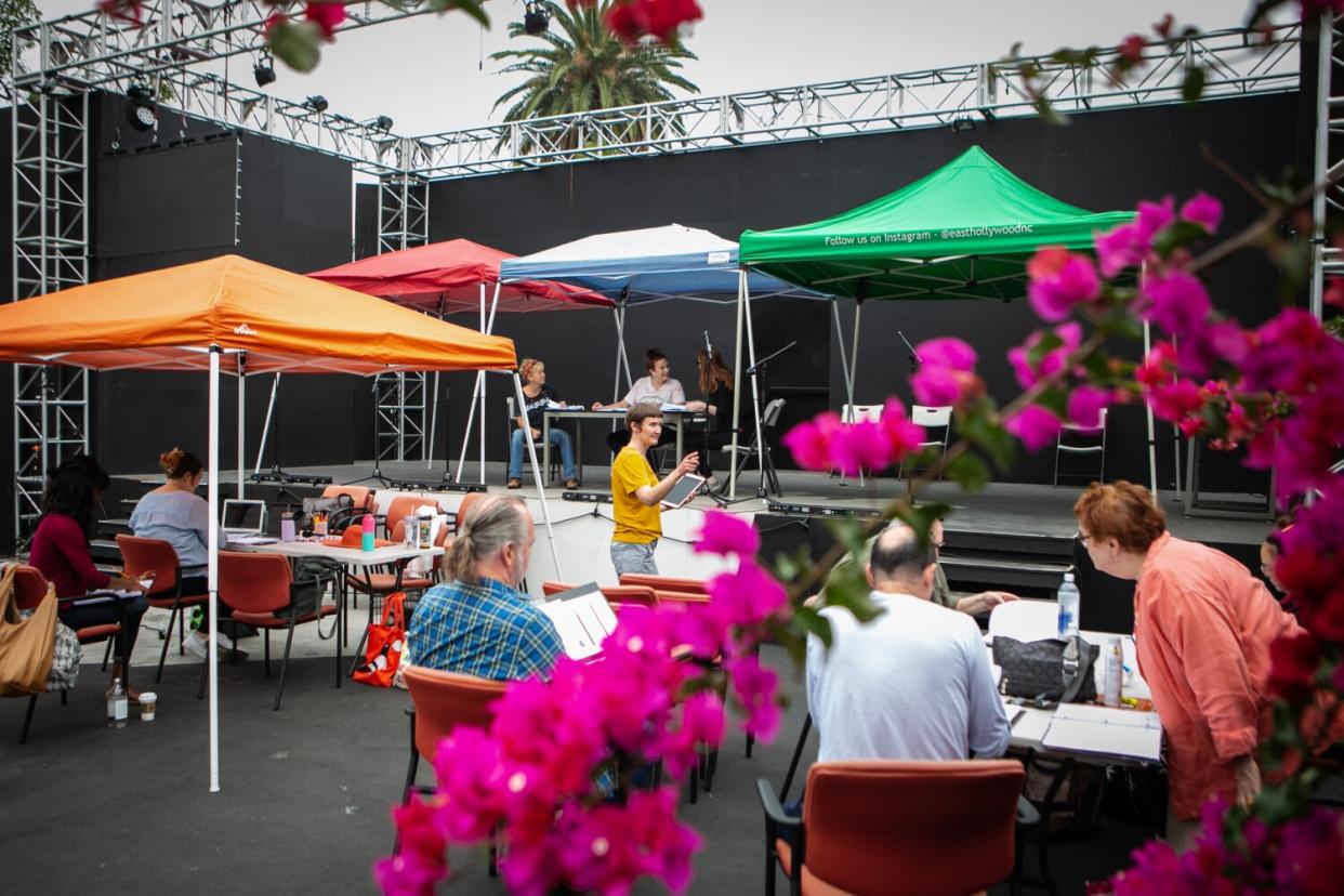 A person in a yellow T-shirt walks among people seated under colorful pop-up tents at the Fountain Theatre's outdoor stage.