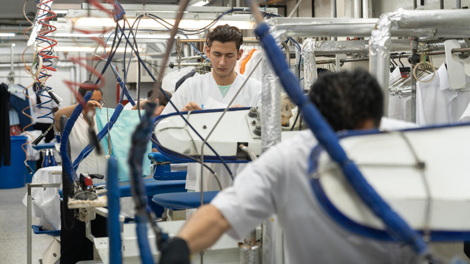 Latin american blue collar workers at an industrial laundry ironing clothes with steamers - Business industry concepts.