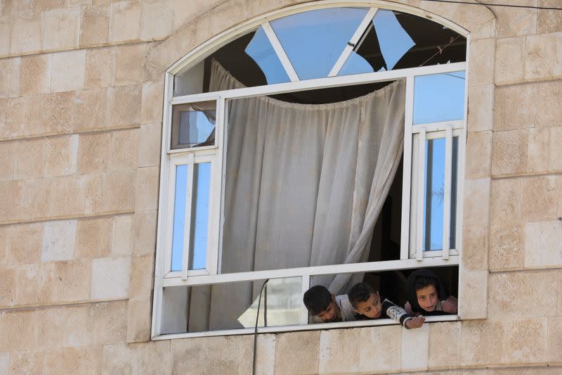 Children look from the window of their apartment in a building near a car workshop hit by a Saudi-led air strike, in Sanaa