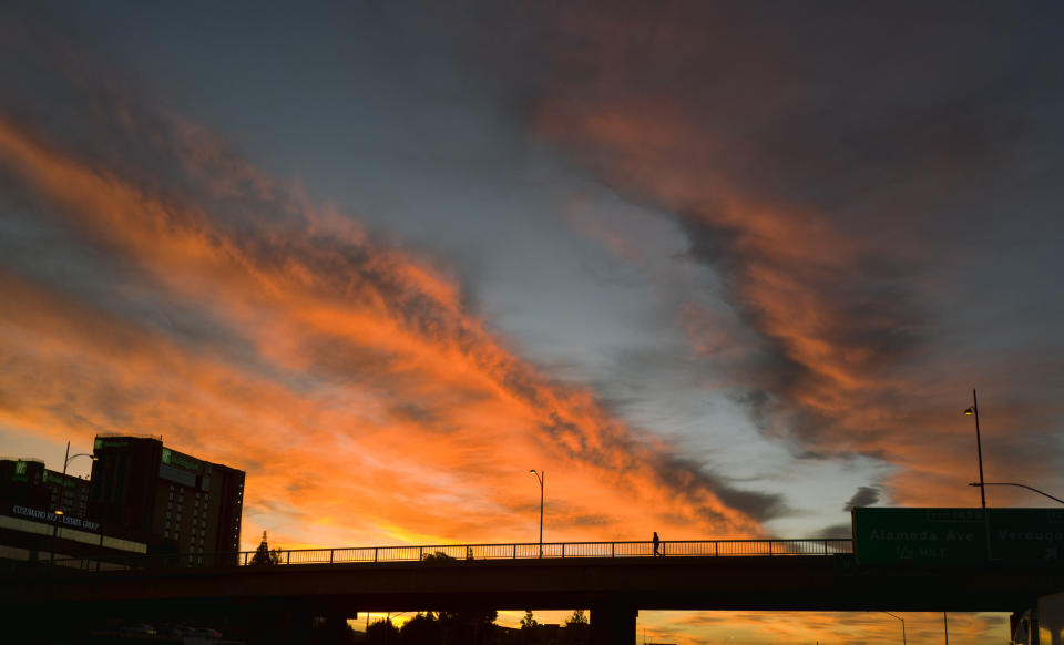 A pedestrian makes their way across an overpass under a dramatic sunrise during the early morning commute in Los Angeles on Friday, Feb. 1, 2019. A powerful storm heading toward California is expected to produce heavy rainfall, damaging winds, localized stream flooding and heavy snow in the Sierra Nevada. Forecasters say rain will arrive in the north late Friday afternoon and reach the south late in the night, and last through Saturday night. (AP Photo/Richard Vogel)