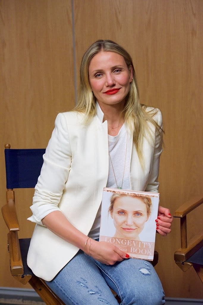 Cameron sitting in jeans and a jacket and holding her "The Longevity Book"