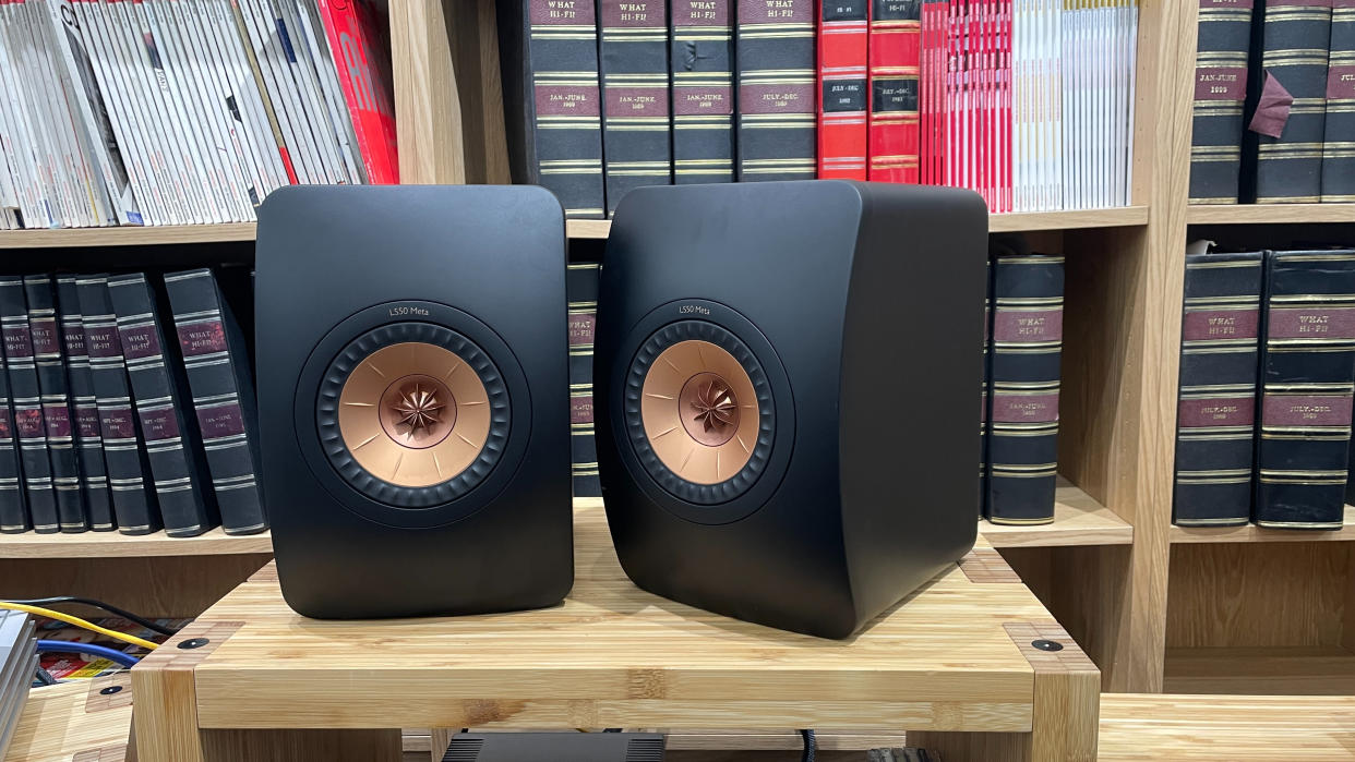  KEF LS50 Meta stereo speakers on wooden equipment rank with books in background. 
