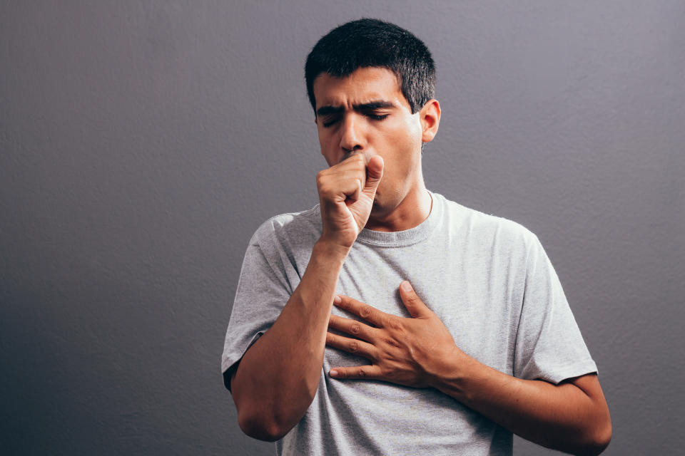 Man coughing into his fist, isolated on a gray background