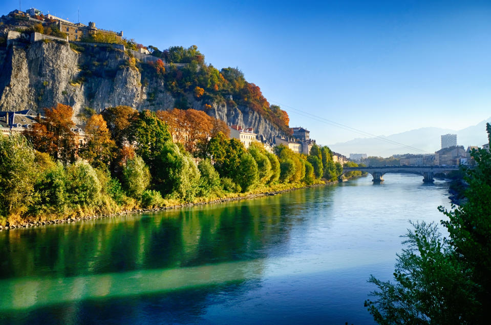 River with a bridge spanning it and a high cliff on the left under a clear sky