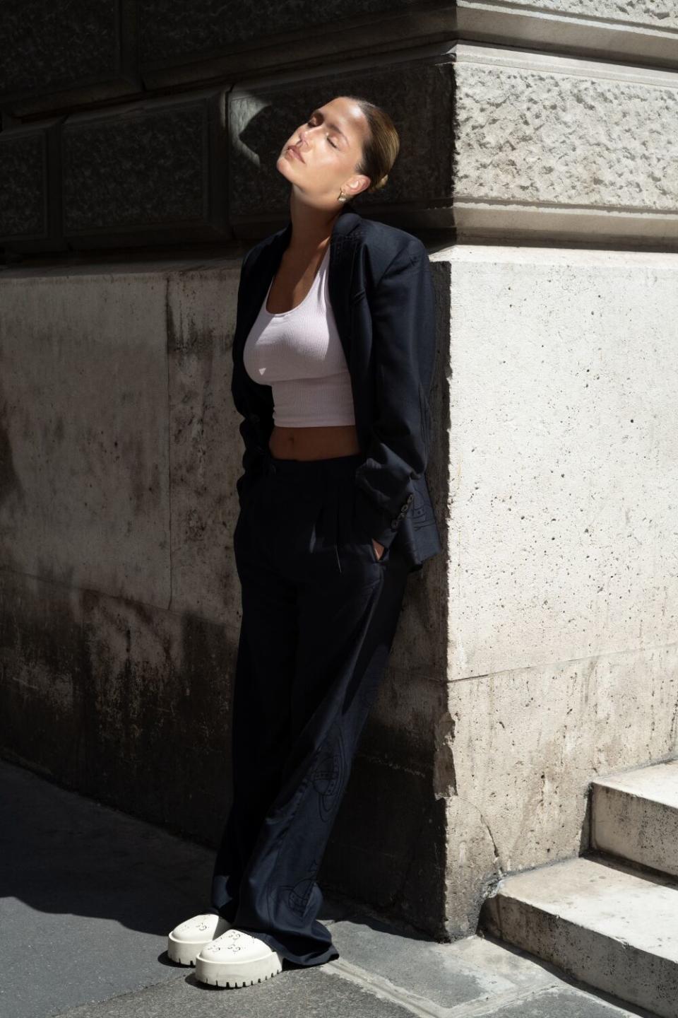 A woman in white sneakers leans against a building