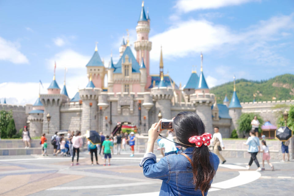 A woman snaps a photo of the Walt Disney Magic Castle.