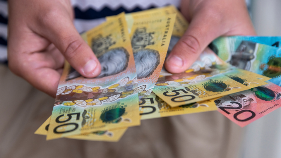 A person holding Australian cash in the form of $50, $20 and $10 notes.