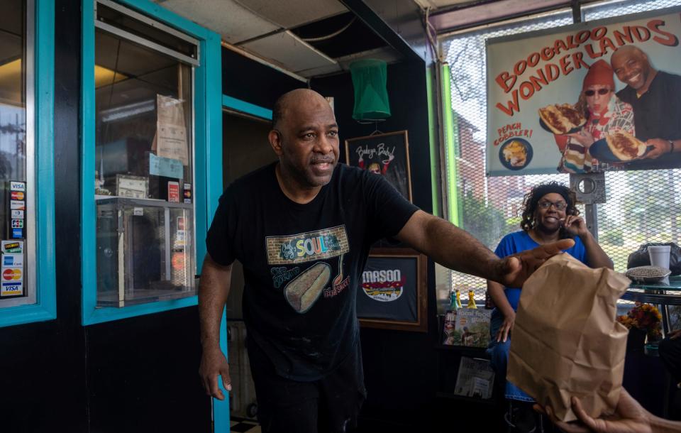 Greg Beard, 62, chef and owner of Soul-N-The Wall, hands an order to a customer as Cheryl Gordon sits behind him inside his restaurant in Detroit on Wednesday, June 21, 2023. 