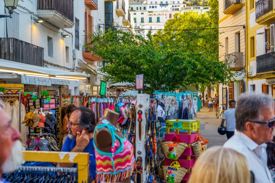 A colorful, busy street in Ibiza with people browsing outdoor shop racks
