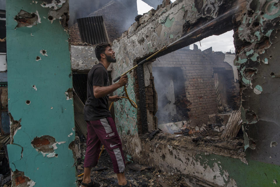 A Kashmiri villager sprays water on burning debris as he clears the house destroyed in a gunfight in Pulwama, south of Srinagar, Indian controlled Kashmir, Wednesday, July 14, 2021. Three suspected rebels were killed in a gunfight in Indian-controlled Kashmir on Wednesday, officials said, as violence in the disputed region increased in recent weeks. Two residential houses were also destroyed. (AP Photo/ Dar Yasin)