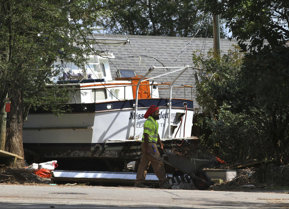 A cleanup crew member pushes a wheelbarrow of storm debris past a beached yacht on East Front Street in New Bern, N.C., Thursday, Sept. 20, 2018. Hurricane Florence brought destructive flooding and storm surge to the historic community near the Neuse River. (Gray Whitley/Sun Journal via AP)