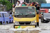 Workers sit on a truck transporting them through a flooded road, at an area affected by land subsidence and rising sea level in North Jakarta