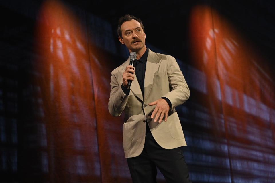 jude law holds a microphone as he speaks at a press event