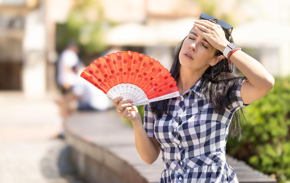 Woman uses hand fan to cool down when summer heat wave hits the city.Hot weather illnesses include heat cramps, heat exhaustion and a heat stroke. (Getty)