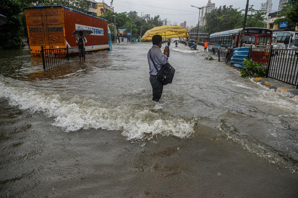 A commuter steadies himself to negotiate flowing water while crossing a flooded road during a heavy monsoon rain in Mumbai on August 4, 2020.(Photo by INDRANIL MUKHERJEE/AFP via Getty Images)