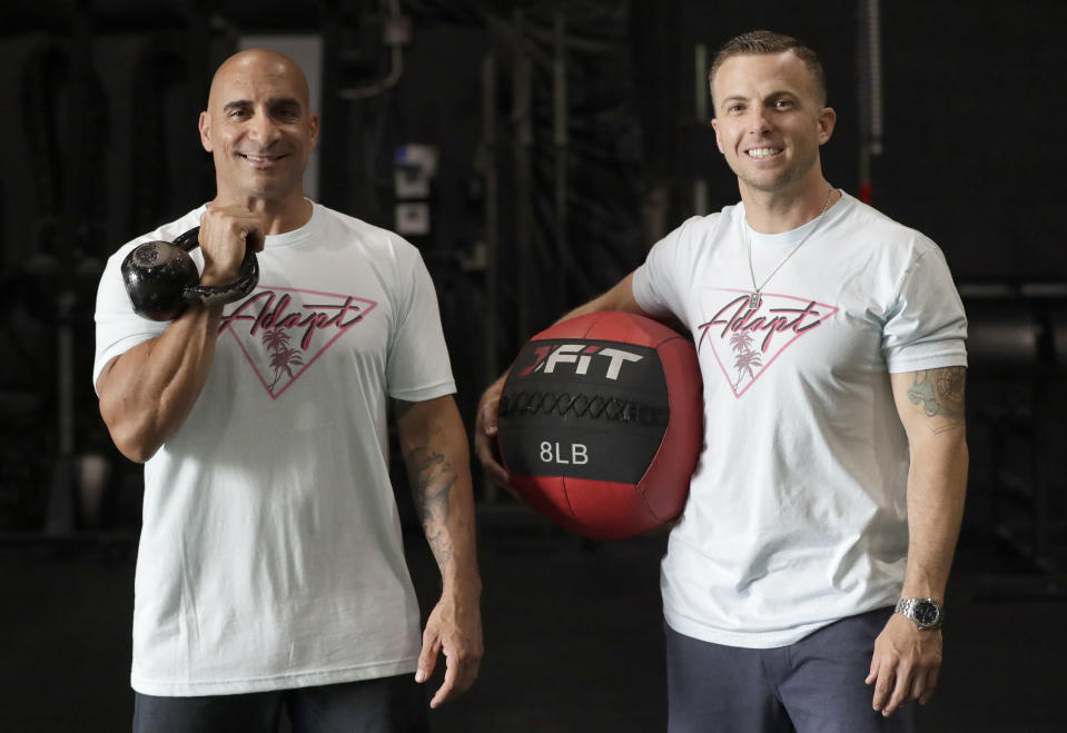 In this Thursday, June 4, 2020, photo, ADAPT gym owners Scott Grondin, right, and Jorge Sanchez pose for a photo at the gym in North Miami, Fla. The business partners and co-founders of the gym just got the OK to reopen their Miami area studio Monday after three months. Desperate to keep their carefully built 15-person team, they gave up their own salaries to keep the entire staff at full pay, relying on them to quickly pivot to online fitness training. (AP Photo/Wilfredo Lee)