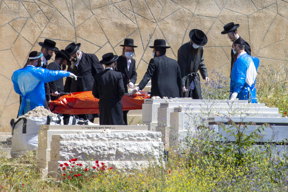In this Friday, May 1, 2020 photo, family and undertakers carry the body of a man who died from the coronavirus in the USA for burial in east Jerusalem's Mount of Olives cemetery. Air travel to Israel has come to a near standstill due to coronavirus restrictions, but one type of voyage still endures: the final journey of Jews wishing to be buried in Israel. Families, the aviation industry and health workers are finding ways to keep the deceased flying in despite the challenges presented by the virus. (AP Photo/Ariel Schalit)