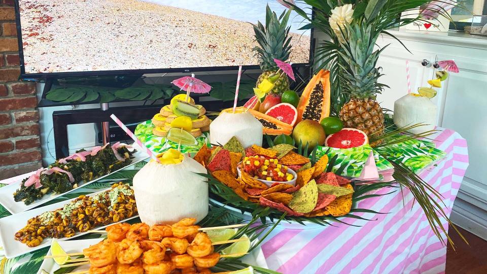 Create a beach-worthy ambiance at home with a dining table filled with tropical fruits, flowers and tasty food. (Photo: Yahoo Life)