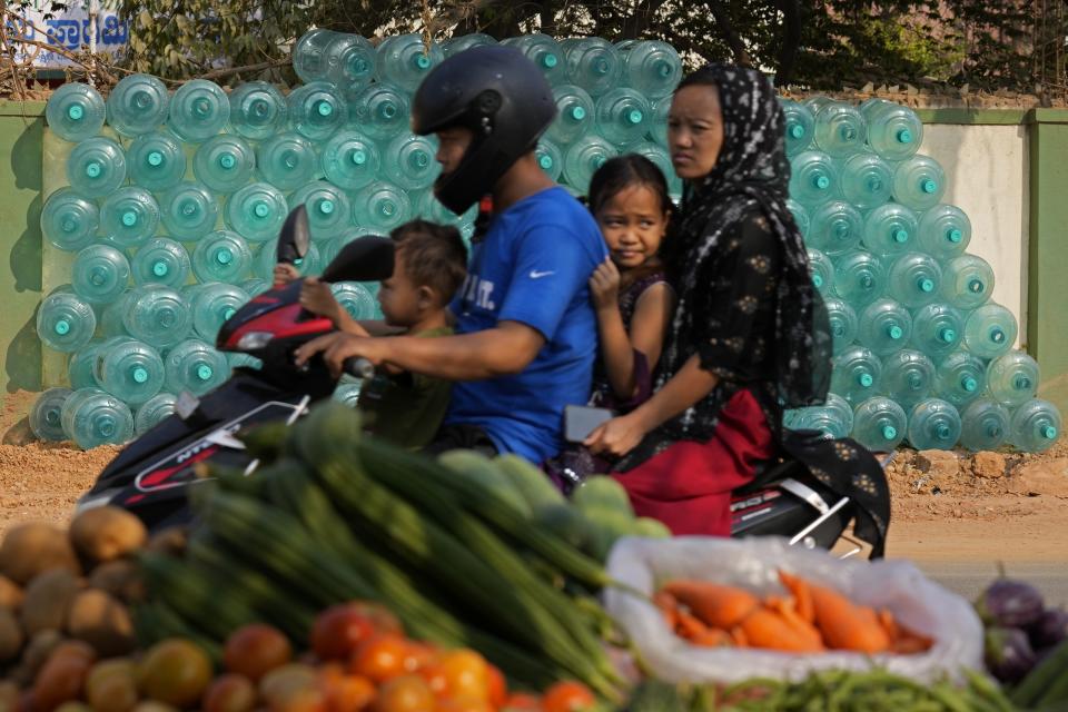 A motorist rides with his family past the stacked empty drinking water cans to be transported for refilling in Bengaluru, India, Monday, March 11, 2024. (AP Photo/Aijaz Rahi)