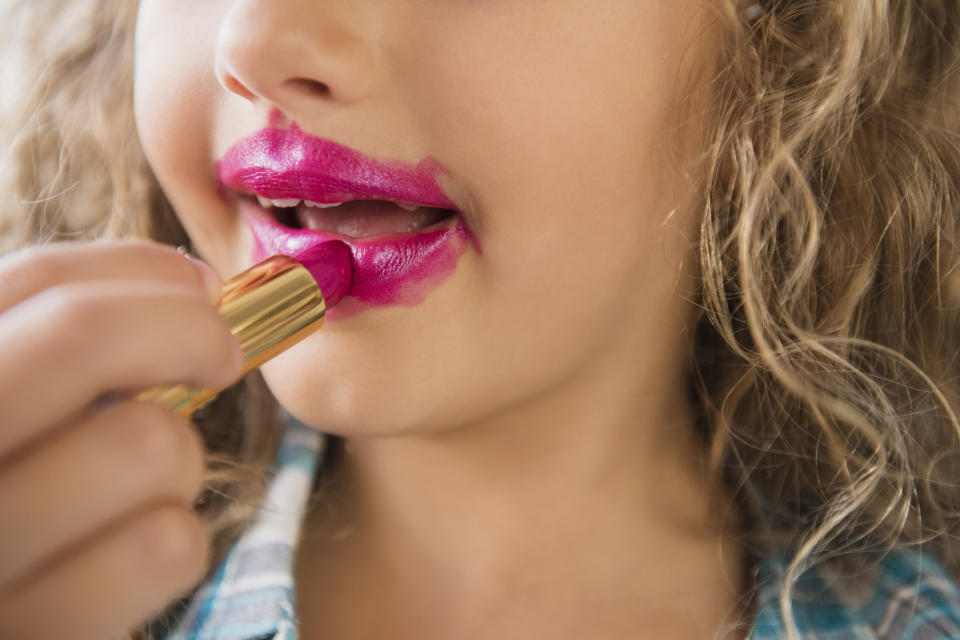 A little girl putting lipstick all over her face