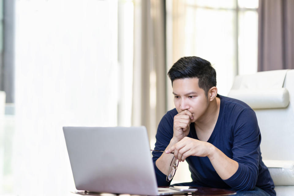 Man at laptop resting hand on chin and holding a pair of eyeglasses while looking serious