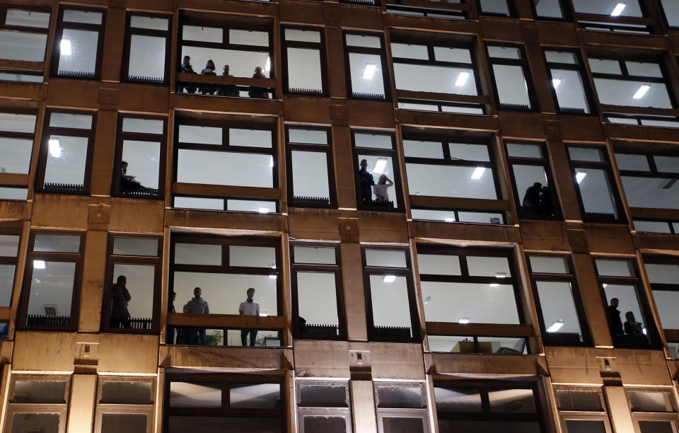 People stand in a building watching a protest in Belgrade, Serbia, Saturday, Dec. 8, 2018. Thousands of people are marched in Serbia against the autocratic rule of President Aleksandar Vucic and his government. An opposition alliance called the protest on Saturday after assailants recently beat up and seriously injured a leftist party leader and his associates in a southern Serbian city. (AP Photo/Darko Vojinovic)