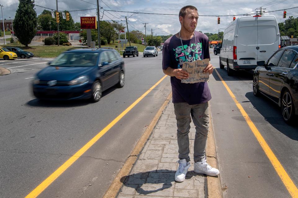 In this file photo from Asheville, N.C., Sean Alcock, who is homeless, stands in the middle of a roadway asking for help from motorists.
