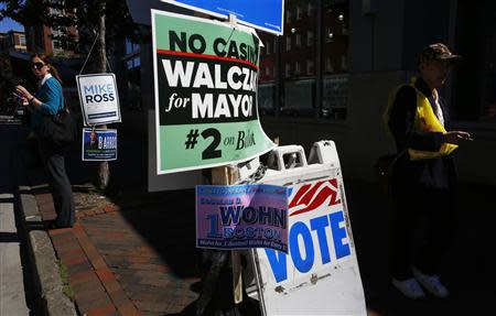 Pedestrians stand and walk amidst campaign signs outside a polling station in Boston, Massachusetts September 24, 2013. REUTERS/Brian Snyder