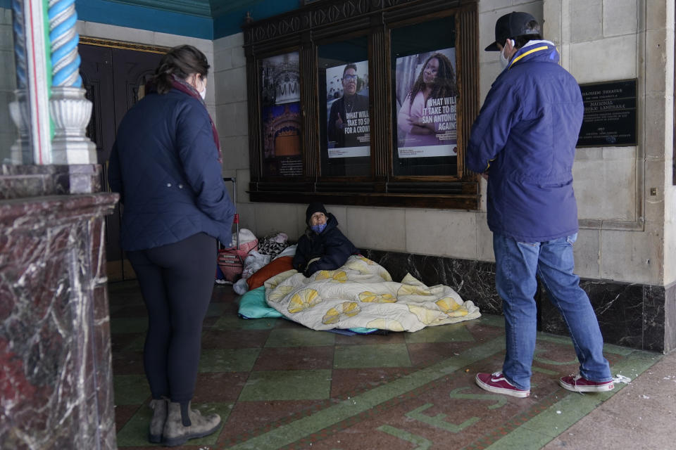 A woman who identified herself as Caroline and using blankets to keep warm outside the Majestic Theater, is encouraged by Morgan Handley, left, and Pastor Gavin Rogers, right, to seek shelter, Tuesday, Feb. 16, 2021, in San Antonio. (AP Photo/Eric Gay)