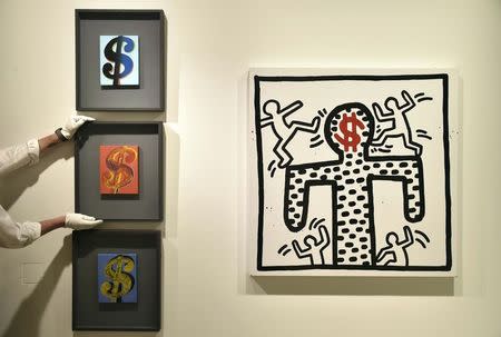 A Sotheby's employee poses with 'Three Dollar Signs' by Andy Warhol (L) and 'Untitled' by Keith Haring (R) at Sotheby's auction house in London June 8, 2015. REUTERS/Toby Melville