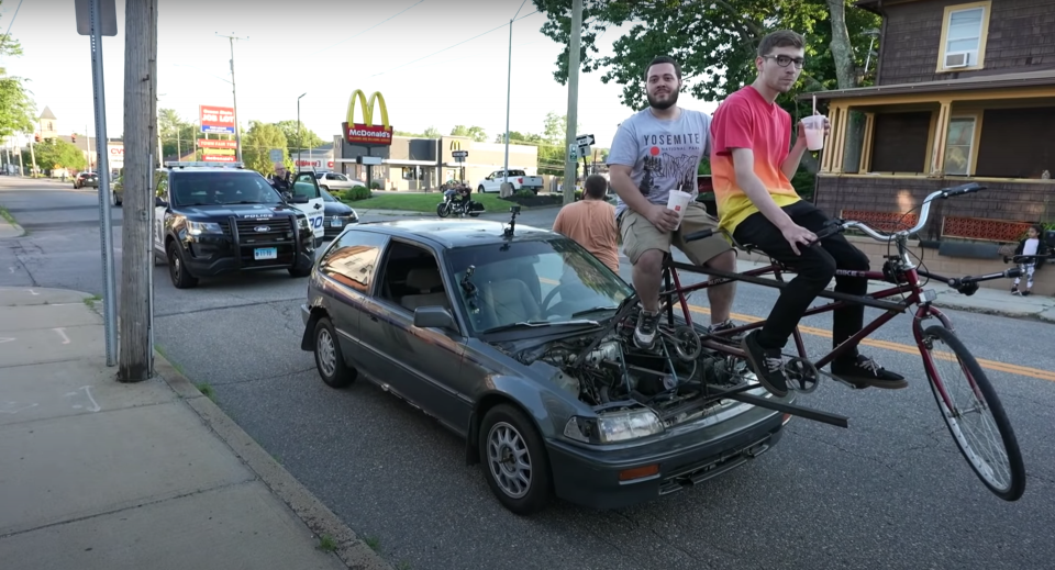 A cop pulls over two men riding a bicycle-car to their local McDonald's.