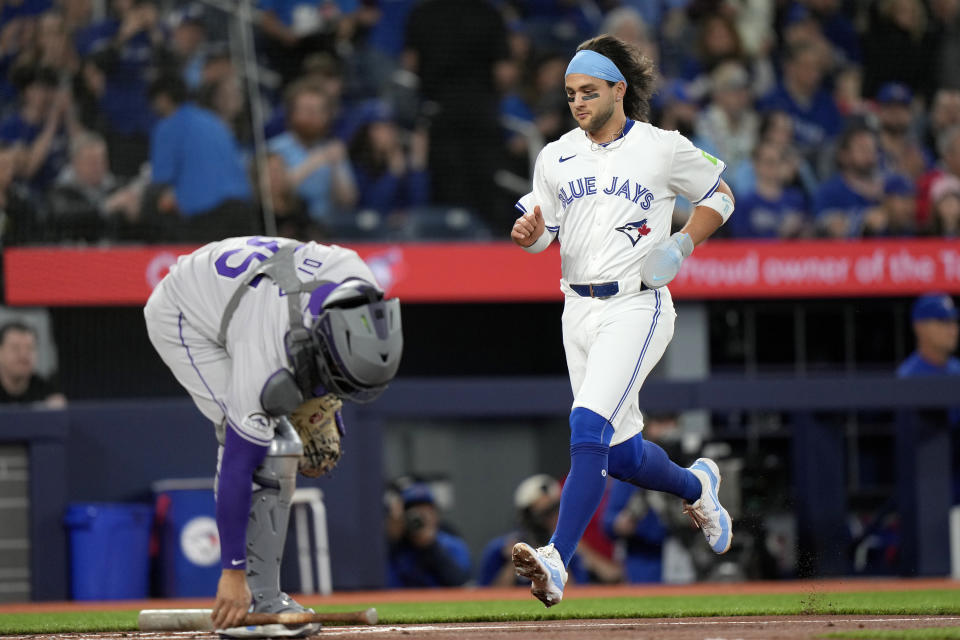 Colorado Rockies catcher Elias Diaz, left, picks up a bat as Toronto Blue Jays' Bo Bichette, right, scores on a single by teammate Cavan Biggio (not shown) during first-inning baseball game action in Toronto, Friday, April 12, 2024. (Frank Gunn/The Canadian Press via AP)