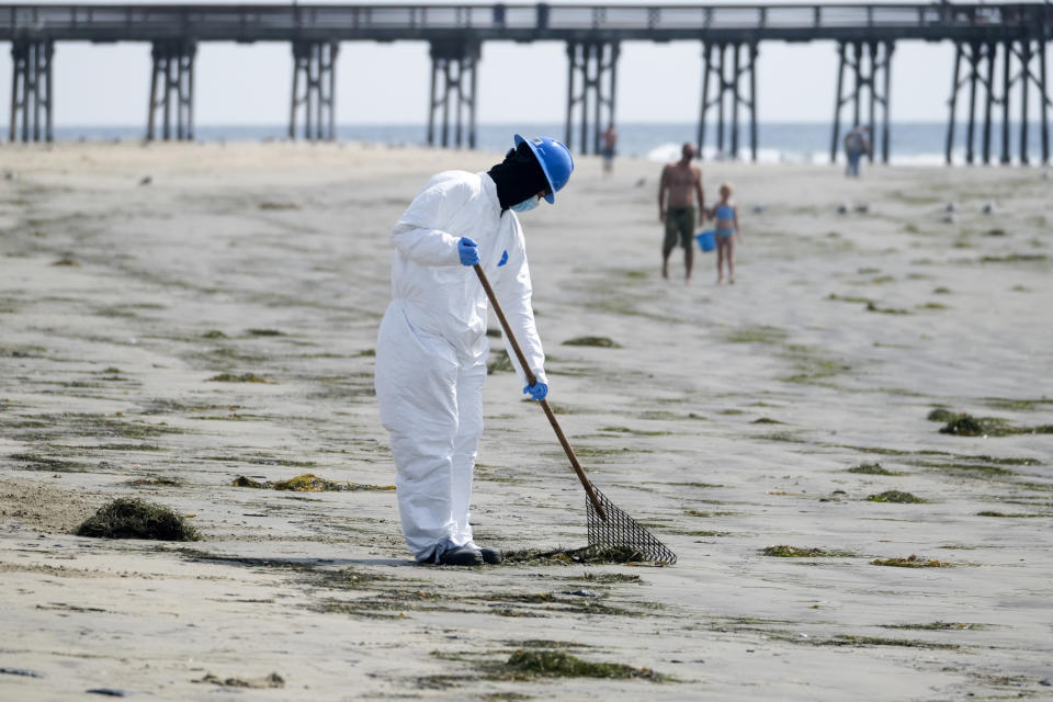 A worker in a protective suit cleans the contaminated beach after an oil spill in Newport Beach, Calif., on Wednesday, Oct. 6, 2021. A major oil spill off the coast of Southern California fouled popular beaches and killed wildlife while crews scrambled Sunday, to contain the crude before it spread further into protected wetlands. (AP Photo/Ringo H.W. Chiu)