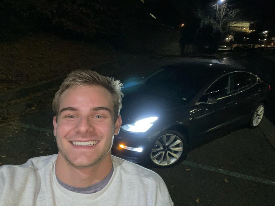 a man takes a selfie with a Tesla in the dark