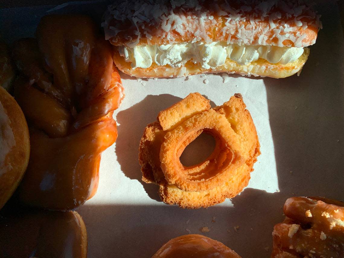 A classic old fashioned at Tacoma’s Dockside Donuts, in a box with popular styles including a coconut angel bar (top) and cinnamon-apple bowtie (left).