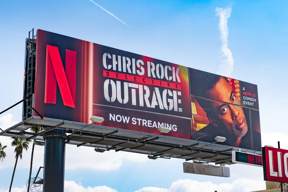 A Netflix billboard promoting Chris Rock's comedy special "Selective Outrage" against a blue sky with white clouds.