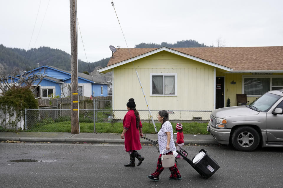 Brenda López Alvarado, left, and Celia Magdaleno walk to their homes after collecting water from their neighbor's pool following an earthquake in Rio Dell, Calif., Wednesday, Dec. 21, 2022. Water service has not return to the city. (AP Photo/Godofredo A. Vásquez)