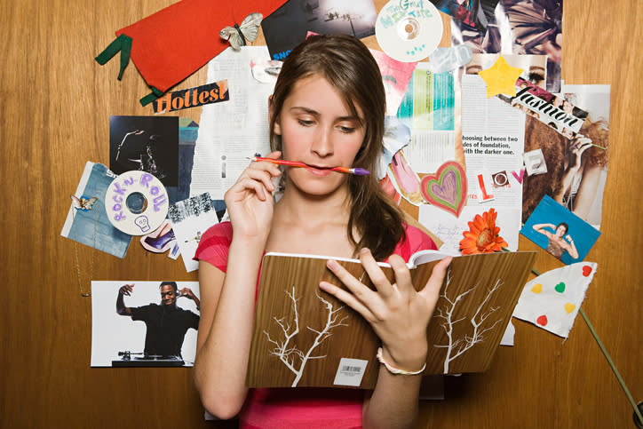 Woman pondering over a book with a cluttered bulletin board behind her