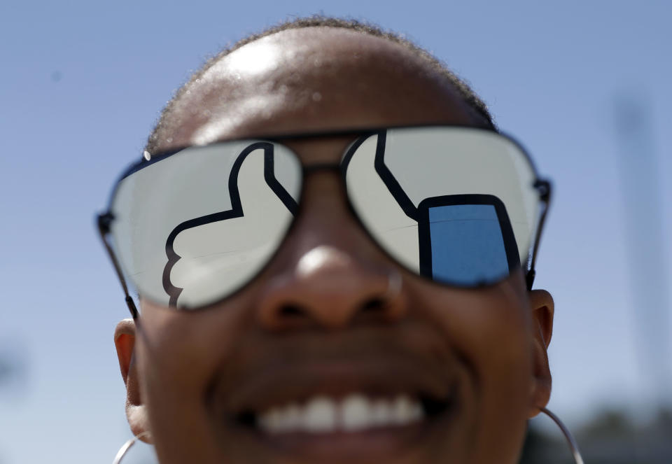 In this March 28, 2018, file photo, a visitor poses for a photo with the Facebook logo reflected on her sunglasses at the company's headquarters in Menlo Park, Calif. Facebook revealed Wednesday, April 4, that tens of millions more people might have been exposed in the Cambridge Analytica privacy scandal than previously thought and said it will restrict the user data that outsiders can access. (AP Photo/Marcio Jose Sanchez)