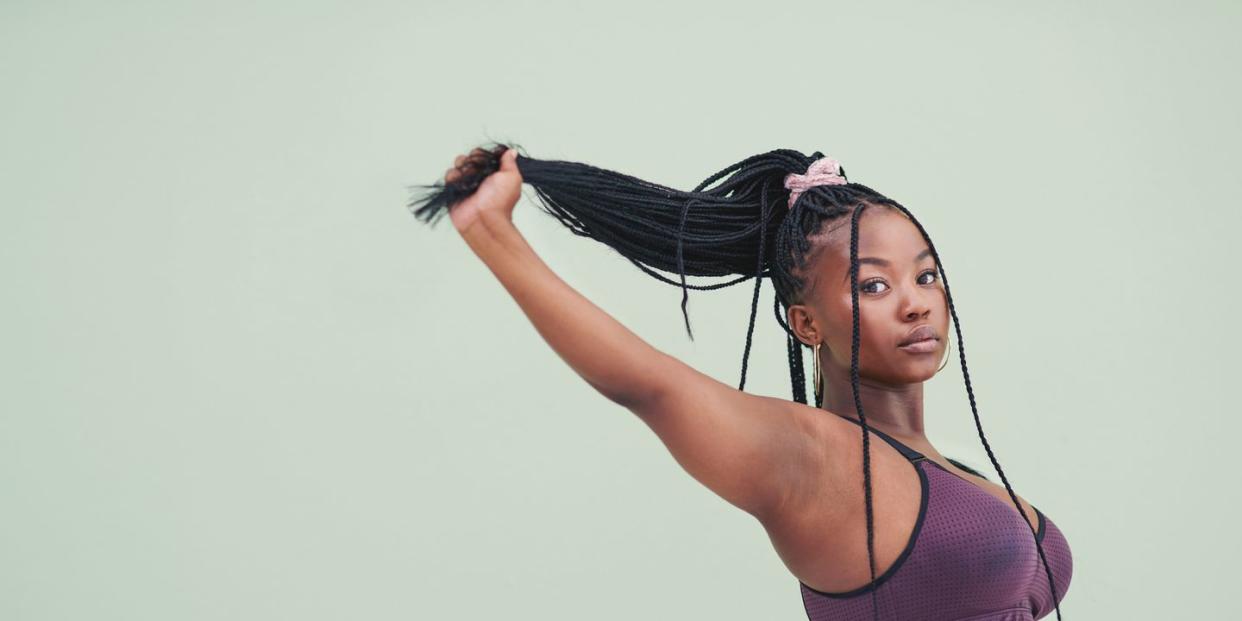 cropped studio portrait of a young woman pulling her hair and posing against a green background