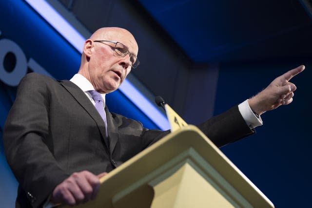 John Swinney at a lectern, pointing off camera