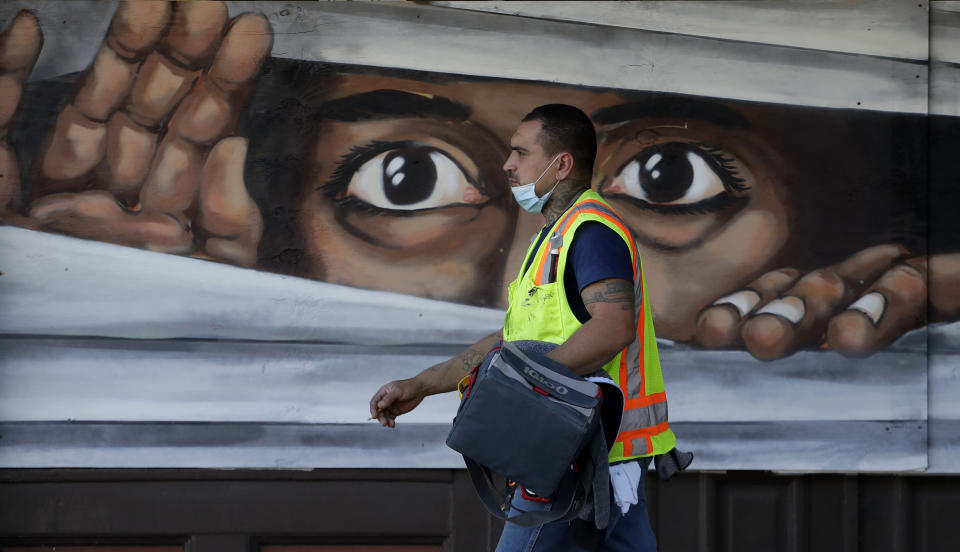 A construction worker walks past a mural painted on a boarded up business that is temporarily closed due to the COVID-19 pandemic Monday, April 27, 2020, in Austin, Texas. Texas Gov. Greg Abbott announced he is relaxing some restrictions that have been imposed on some businesses. (AP Photo/Eric Gay)