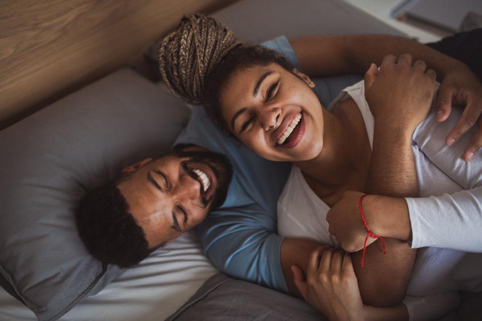 portrait of young couple playing on bed indoors at home, laughing at funny good morning message