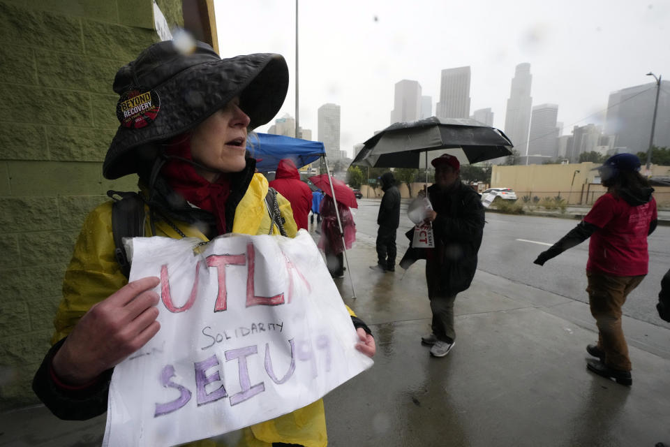 Los Angeles Unified School District, LAUSD teacher Sarah Phillips, left, stands under heavy rain outside the closed doors of the Edward R. Roybal Learning Center in Los Angeles, Tuesday, March 21, 2023. Tens of thousands of workers in the Los Angeles Unified School District walked off the job Tuesday over stalled contract talks, and they were joined by teachers in a three-day strike that shut down the nation’s second-largest school system. (AP Photo/Damian Dovarganes)